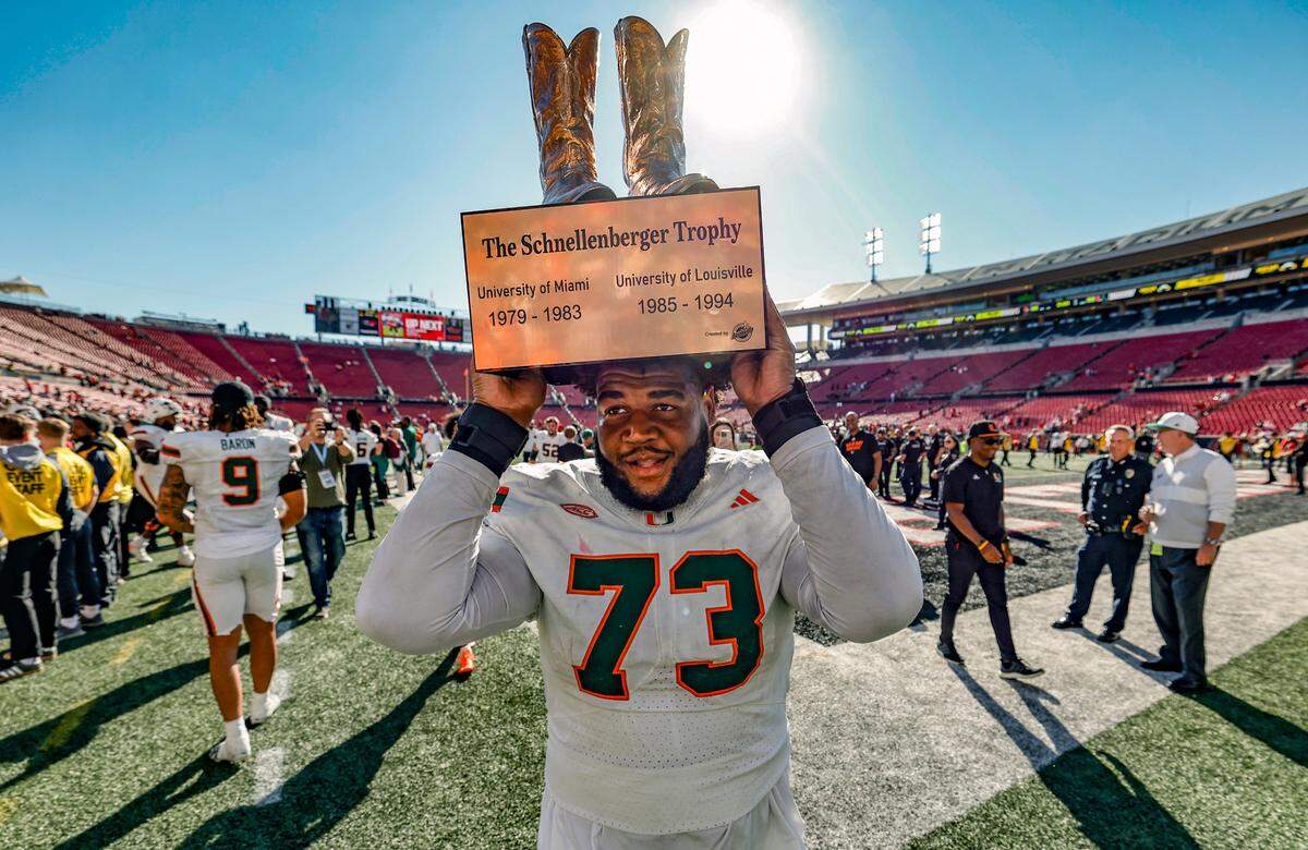 Miami Hurricanes offensive lineman Anez Cooper (73) carries the Howard Schnellenberger trophy as the Canes win the rivalry game against the Louisville Cardinals in an NCAA football game at L&N Federal Credit Union Stadium in Louisville, Kentucky on Saturday, October 19, 2024. 