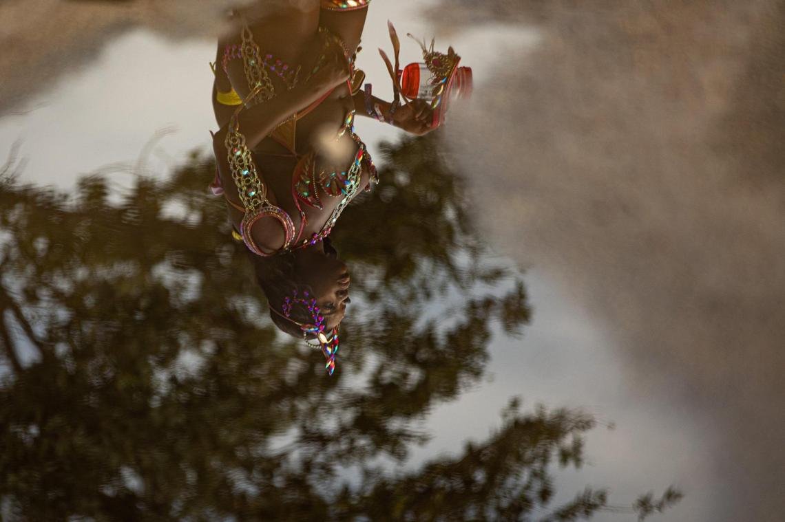 A reflection of a performer is seen as she walks across a parking lot during Miami Carnival at the Miami-Dade County Fair Expo in Miami, Florida on Sunday, October 9, 2022.