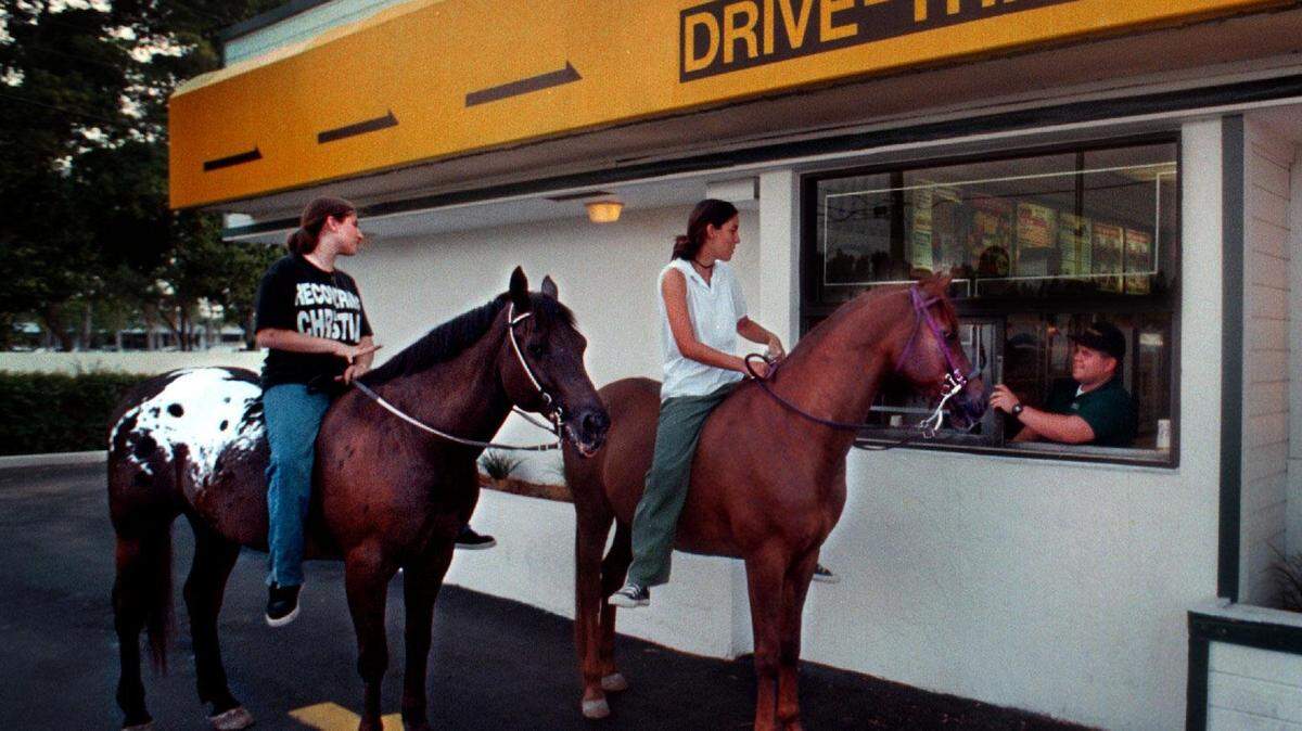 Eating while driving could be covered by distracted driving laws. Usually that focuses on cars and not horses. In this 1997 file photo, customers on horseback visit a Davie drive-thru.