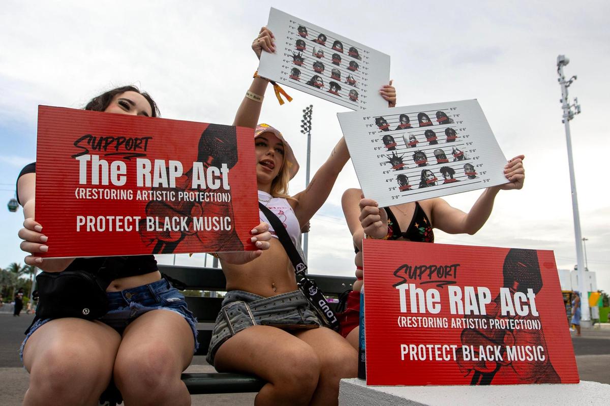 From left to right, festvial attendees Dani Green, 22, Grace Danjou, 22, and Georgia Jones, 21, react with signs supporting the RAP ACT before a townhall to educate attendees about the Restoring Artistic Protection Act (RAP Act) on day one of Rolling Loud Miami 2023 at Hard Rock Stadium in Miami Gardens, Florida, on Friday, July 21, 2023.