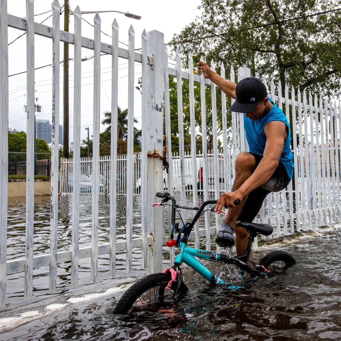A man attempts to stay dry while dragging his bike along Eighth Avenue in the Little Havana neighborhood of Miami, Florida, on Saturday, June 4, 2022.
