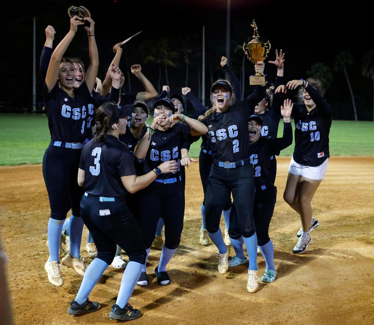 Coral Springs Charter softball team celebrates after defeating Western in the BCAA Big 8 softball championship game at Pompano Beach Community Park in Pompano Beach on Thursday, April 27, 2023. Holding the championship trophy is Alivea Taigl (2).