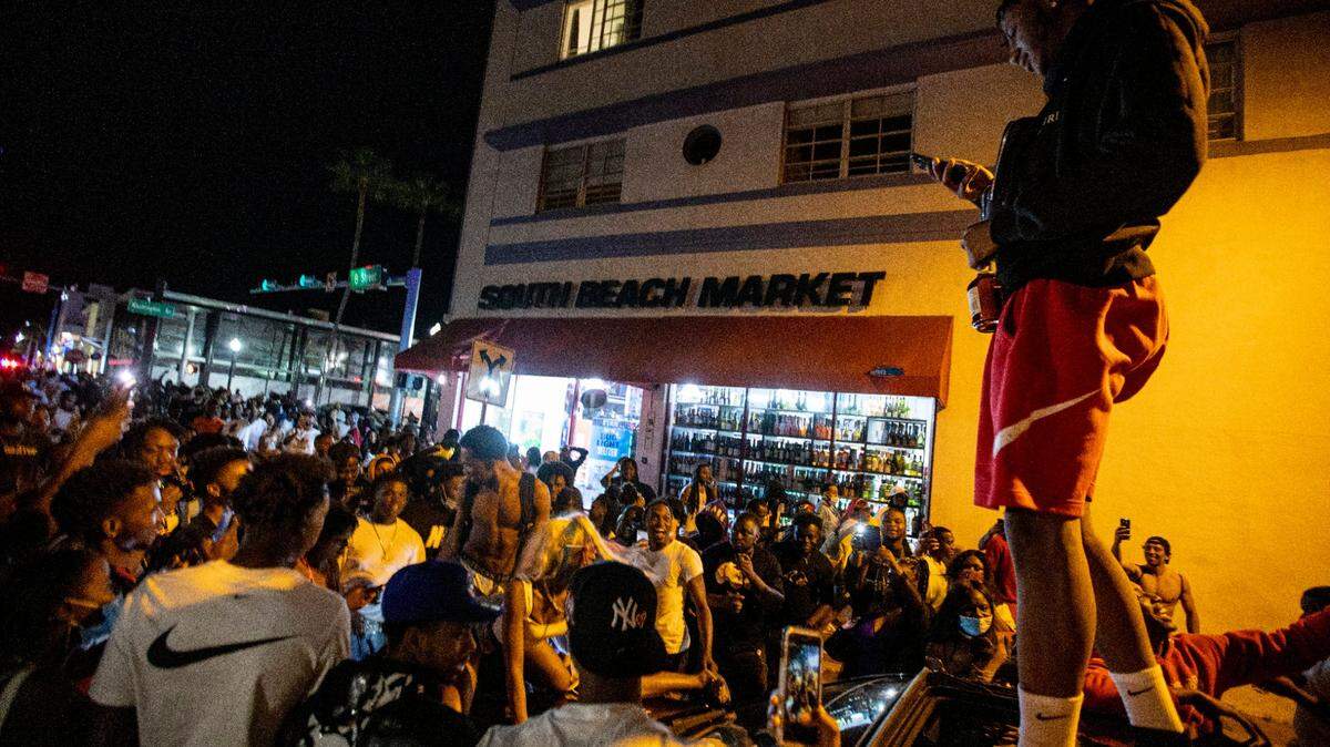A man stands on a car as crowds defiantly frolic in the street while a speaker blasts music an hour past curfew at the corner of Eighth street and Washington Avenue, in Miami Beach, Florida, on Sunday, March 21, 2021. As Miami Beach Police closed down Ocean Drive, roves of people moved west toward Alton Road before a few arrests broke up the crowd.