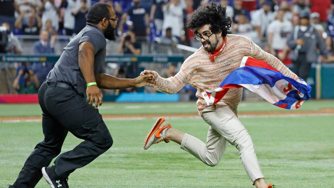 A protester carrying a Cuban flag with the words ‘Patria y Vida’ is chased by security on the field during the game between the United States and Cuba at the World Baseball Classic semifinal at loanDepot park in Miami, Fla. on Sunday, March 19, 2023.