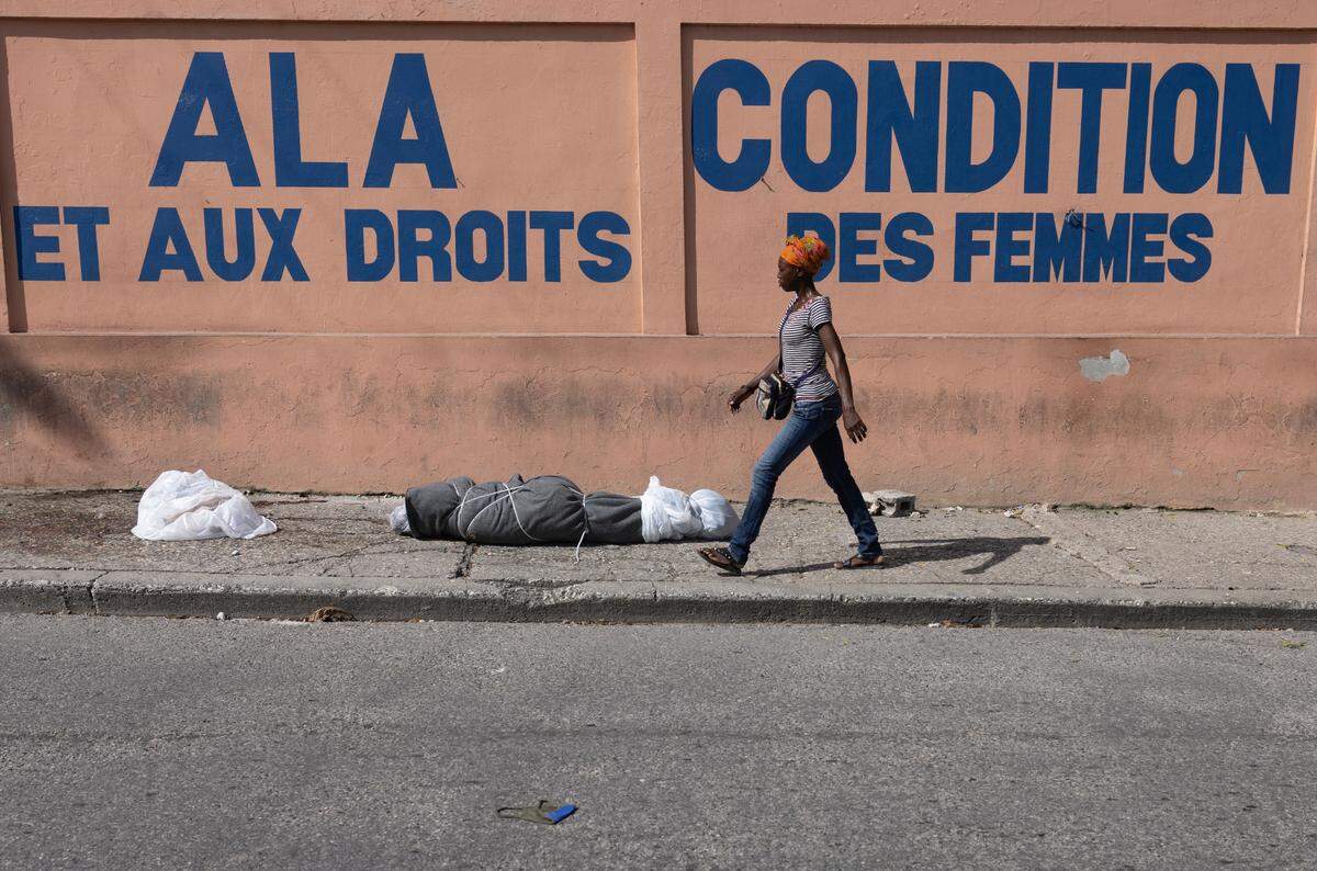 A woman walks next to the body of a woman who was killed, according to local media, by gang members in downtown Port-au-Prince on May 27, 2024.