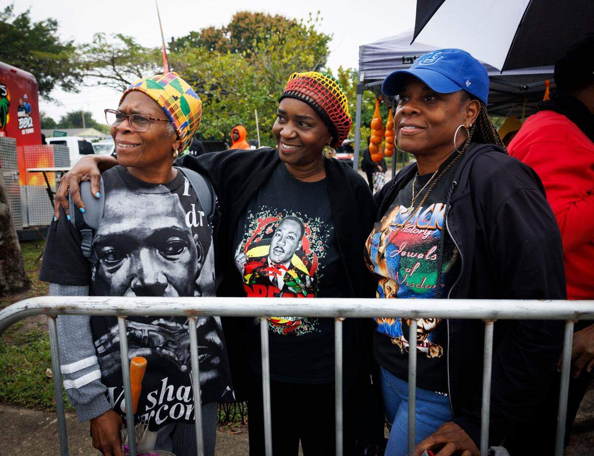 Roseshell Sampson, left, Sharon McKinney, center, and Tierney Gaines smile while watching the Dr. Martin Luther King Jr. Day parade pass by on Monday, Jan. 20, 2025, in Liberty City in Miami, Fla. “Rain or shine we gotta keep the Dream alive,” said Sampson.