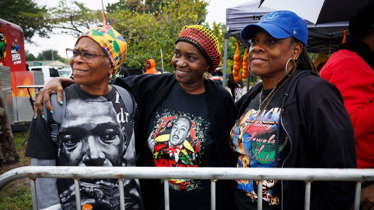 Roseshell Sampson, left, Sharon McKinney, center, and Tierney Gaines smile while watching the Dr. Martin Luther King Jr. Day parade pass by on Monday, Jan. 20, 2025, in Liberty City in Miami, Fla. “Rain or shine we gotta keep the Dream alive,” said Sampson.