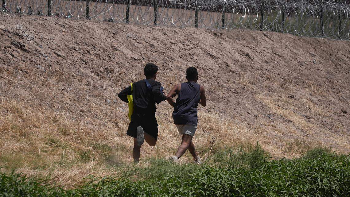 In this file photo, two young migrants from Venezuela walk along the Rio Bravo River hoping to cross the barbed wire fence into the United States.