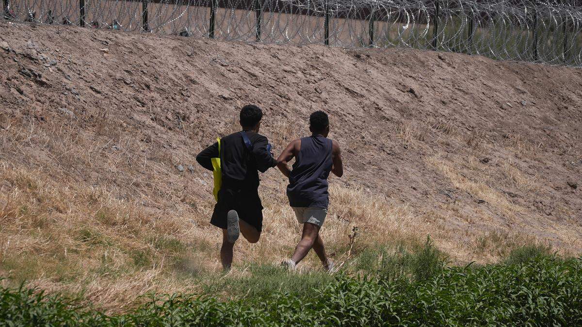 Two young migrants from Venezuela walk along the Rio Bravo River hoping to cross the barbed wire fence into the US on May 11, 2023.