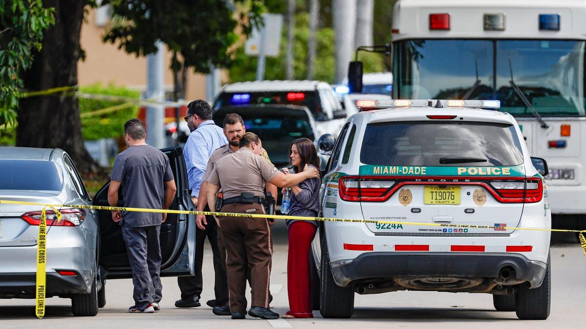 Police console a person on the scene where two adults and one child were shot and killed in a murder suicide at a Chase Bank branch in the Meadows shopping center in West Kendall, Florida, on Friday, June 7, 2024.
