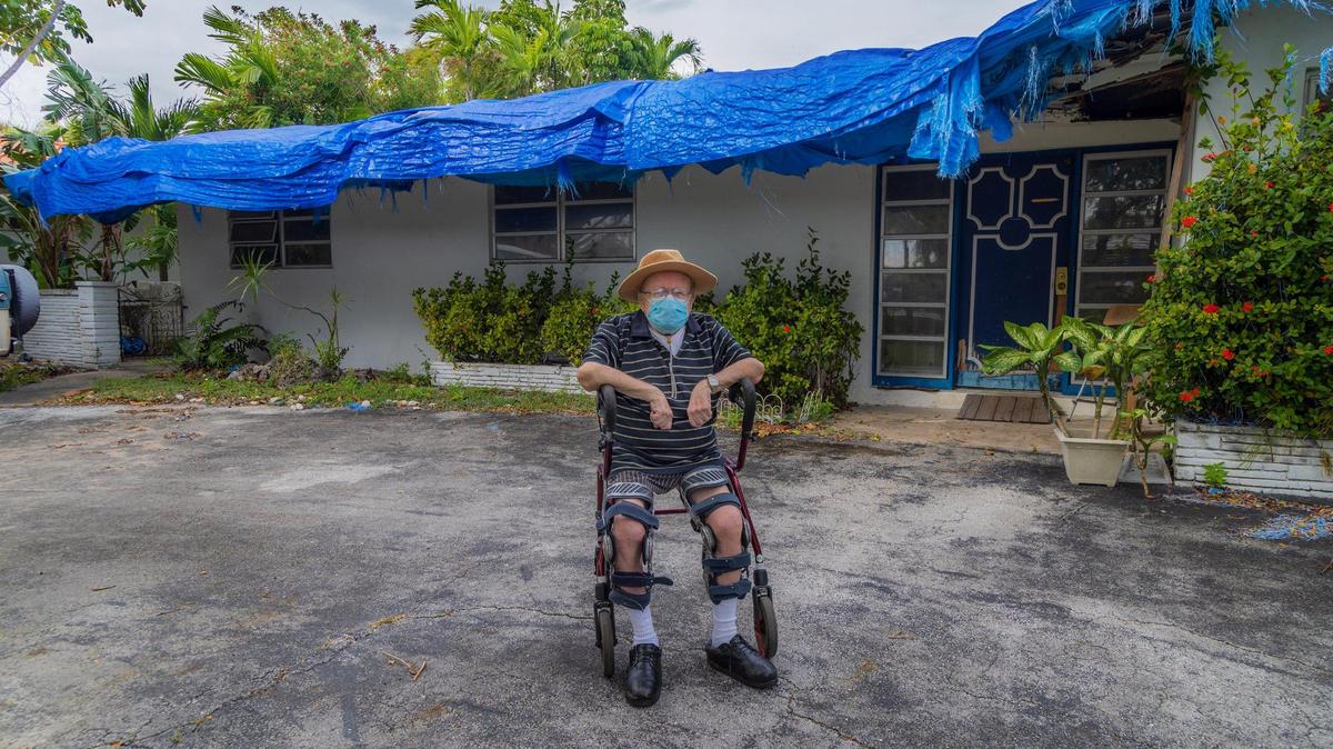 El veterano Kenneth Heller, de 78 años, sentado en un andador frente a su casa en North Miami, el jueves 21 de diciembre de 2023. La casa, con una lona azul cubriendo todo el techo debido a la falta de recursos para arreglarlo, ya que vive de un ingreso fijo y sin dinero extra para arreglar los deterioros.