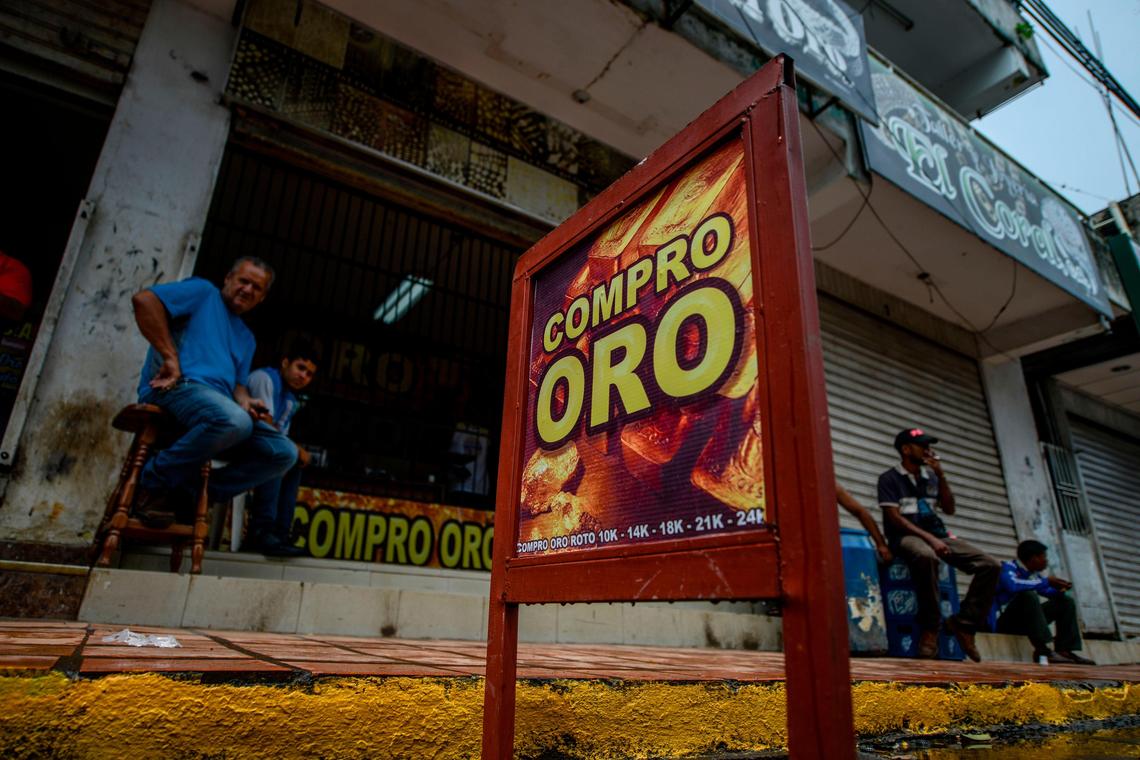 Men sit outside a store whose sign reads ‘We buy gold’ in El Callao, Bolívar state, Feb. 25, 2017. The mining industry supports a massive economy, much of it underground, that spills over into neighboring Colombia, thus disguising the origin of freshly mined gold. From there, the Venezuelan gold often finds its way into the United States, frequently through Miami.