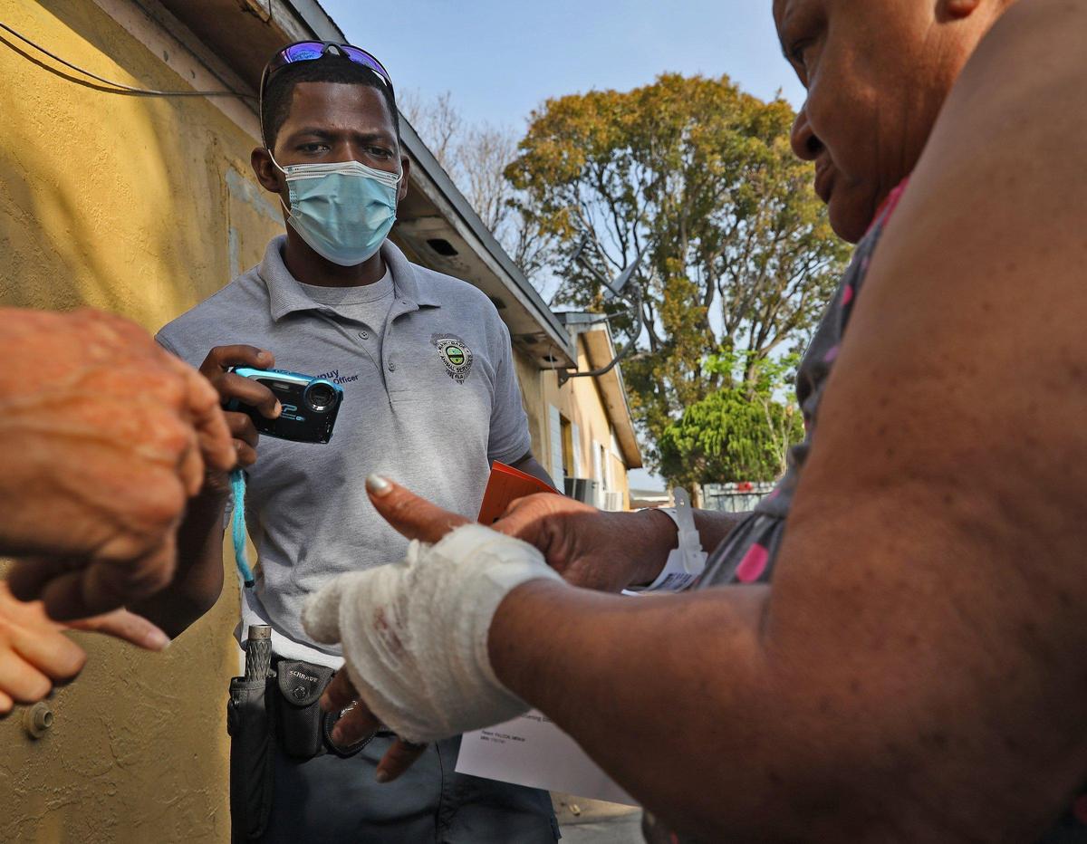 Garson Dupuy, left, a longtime Miami-Dade County animal welfare officer, prepares to take a photo of Miriam Falcon’s injured hand, which she alleges was bitten by her neighbor’s dog, Rocky, at the South Miami Heights multi-rental home on Monday, April 20, 2020.