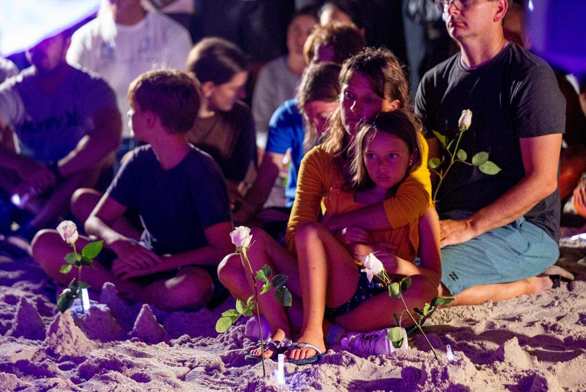 People hold roses and glow sticks during the community beach vigil for those missing and deceased after the partial collapse of the Champlain Towers South condo building. They gathered behind Four Seasons Hotel at The Surf Club in Surfside, near Miami Beach, Florida, on Monday, June 28, 2021.