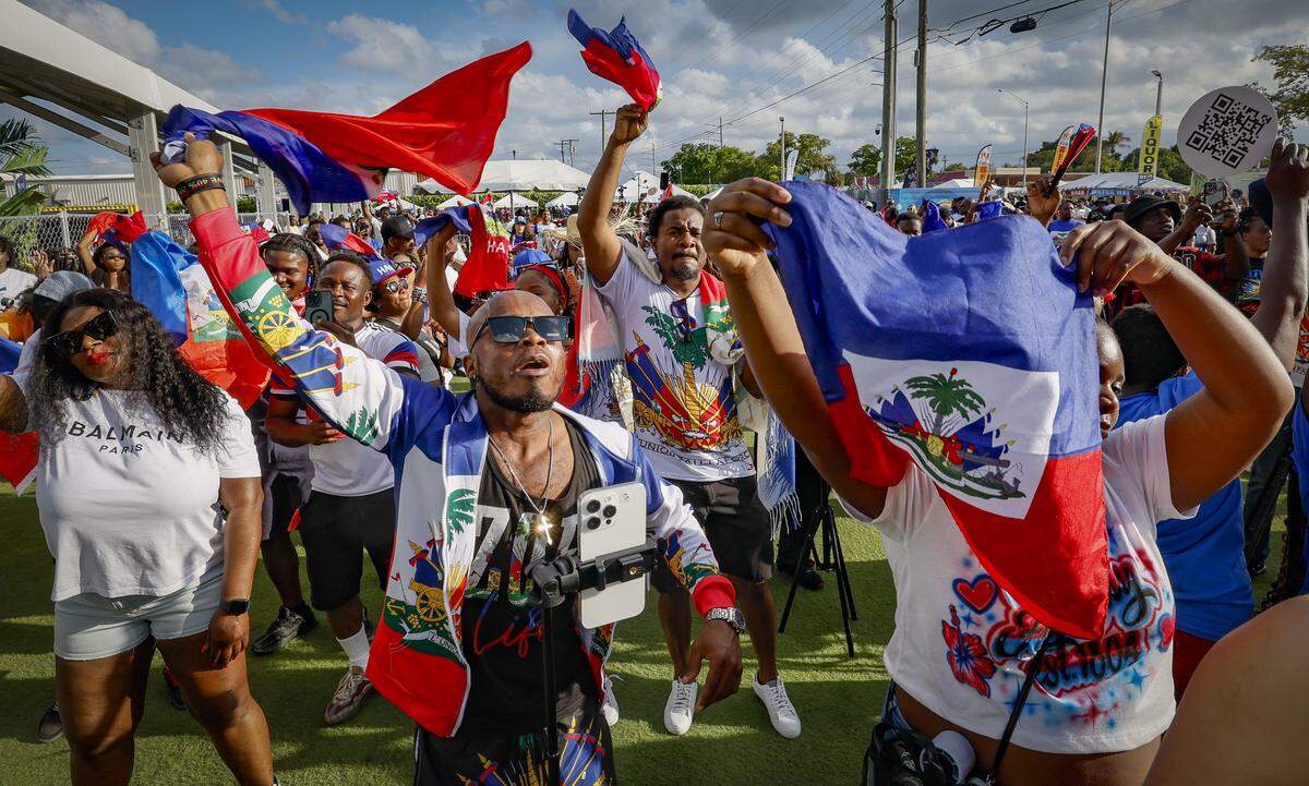 Brucely Ulysse dances and waves a Haitian flag along with others as they listen to performers sing on stage during the 28th Annual Haitian Compas Festival at The NoMI Village celebrating Haitian Flag Day, in North Miami, Florida on Saturday, May 16, 2026.