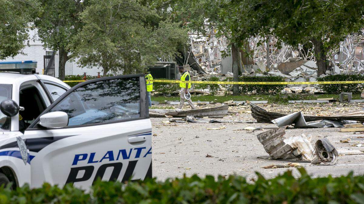 A cleanup crew walks through the parking lot at the Fountains Plaza on Sunday, July 7, across the street from the explosion that happened the day before and injured 23 people.