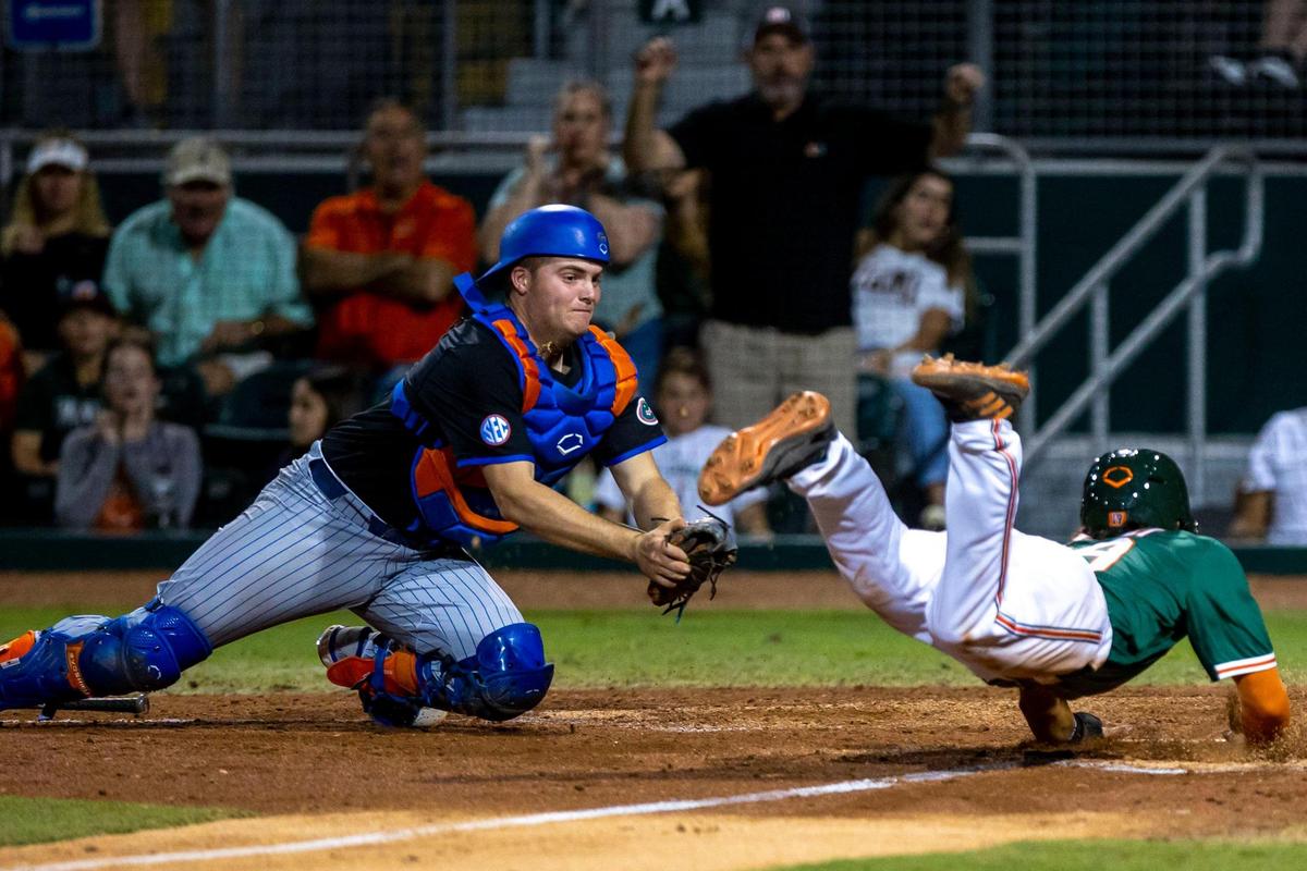 University of Miami base runner Dominic Pitelli (19) dives into home plate before being tagged out by University of Florida catcher Mac Guscette (9) during the fifth inning of an NCAA baseball game inside Alex Rodriguez Park at Mark Light Field in Coral Gables, Florida, on Friday, March 4, 2022.