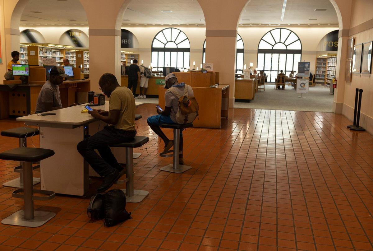 People charge their phones in the air conditioning on Monday, July 17, 2023, at a Miami-Dade Public Library branch in Downtown Miami.