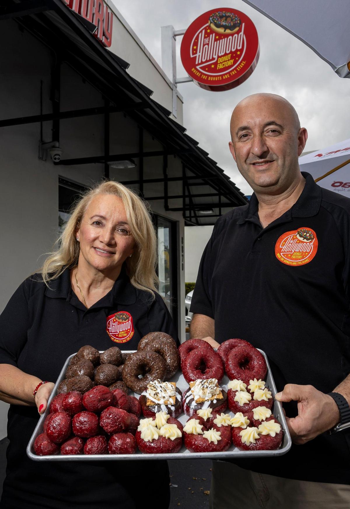 Owners Kat Palushaj and Bobby Palushaj show off red velvet doughnuts and the shop’s new sign on Bird Road in Miami.