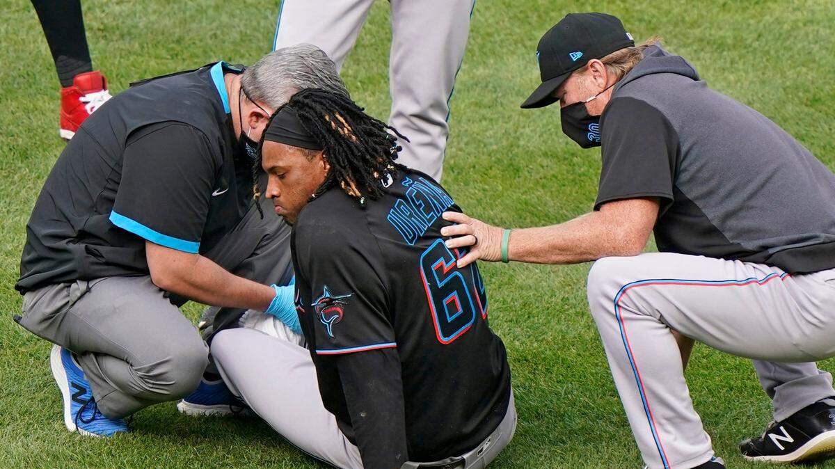 A trainer tends to Miami Marlins starting pitcher Jose Urena (62) who sits on the grass behind home plate after being hit by ball during the third inning of a baseball game against the New York Yankees, Sunday, Sept. 27, 2020, at Yankee Stadium in New York. Marlins pitching coach Mel Stottlemyre, right, looks on. (AP Photo/Kathy Willens)
