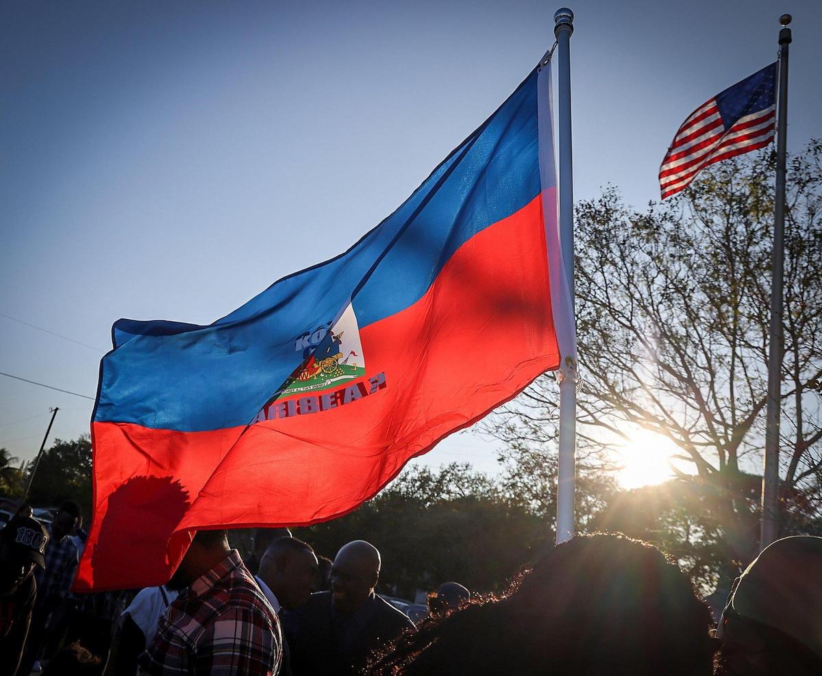 A large Haitian flag waves with the setting sun as members of the Haitian community and others gathered at Toussaint L’ Ouverture Statue for the customary moment of silence occurring at 4:53PM – the time of the 2010 earthquake prior to leading a procession to the Little Haiti Cultural Complex for a ceremonial remembrance of those who perished on Sunday, December 12, 2025.
