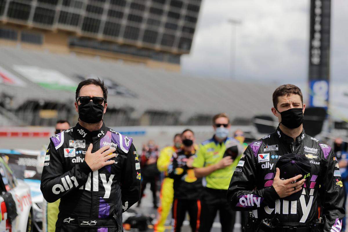 Jimmie Johnson, left, and crew members stand in pit row during the national anthem before a NASCAR Cup Series auto race at Atlanta Motor Speedway, Sunday, June 7, 2020, in Hampton, Ga. (AP Photo/Brynn Anderson)