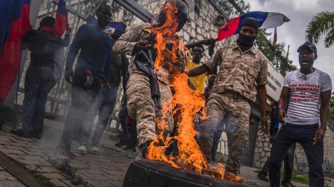 A police officer kicks a burning tire out of the way, in front of the Canadian embassy as demonstrators protest to reject an international military force requested by the government in Port-au-Prince, Haiti, Monday, Oct. 24, 2022.