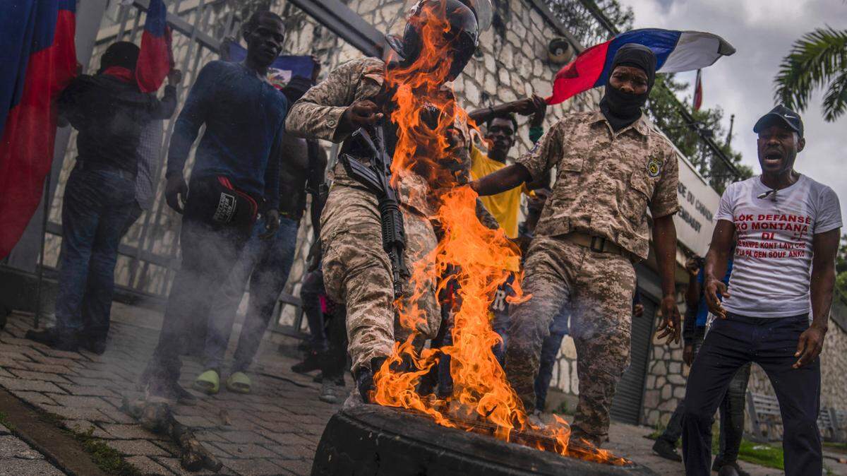 A police officer kicks a burning tire out of the way, in front of the Canadian embassy as demonstrators protest to reject an international military force requested by the government in Port-au-Prince, Haiti, Monday, Oct. 24, 2022.