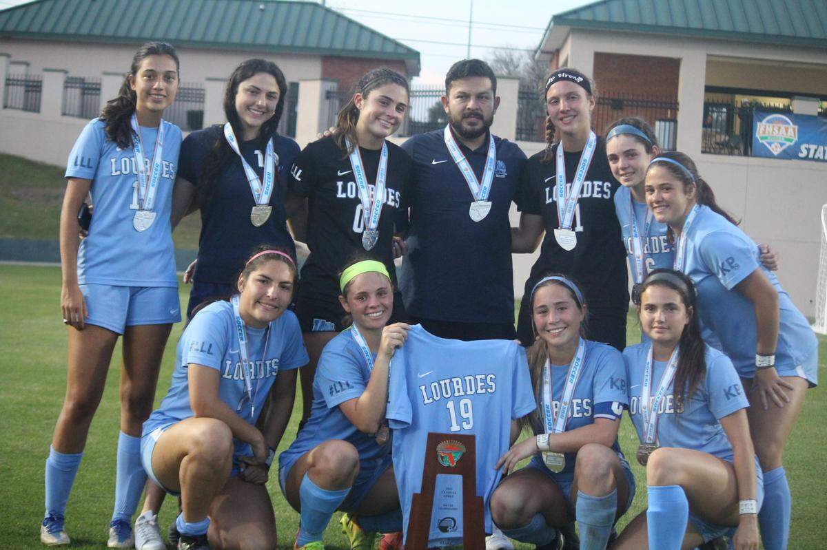 Lourdes players including seniors Rebecca Sampedro and Coco Aguilar (bottom row) holding their teammate, Katy Puig’s No. 19 jersey, pose with the state runner-up trophy following a 4-1 loss to Gulf Breeze Friday afternoon in the Class 6A state girls’ soccer championship match in DeLand.