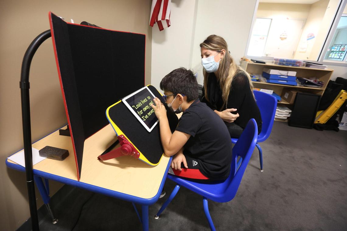 Miami Lighthouse for the Blind and Visually Impaired second-grade student, Lorenzo, works with Francesca Crozier-Fitzgerald, the director of the CVI Collaborative Center and teacher of the visually impaired at the school, on Dec. 6, 2021. Lorenzo was reading a story aloud using an iPad with enlarged, bright yellow letters on a black background.