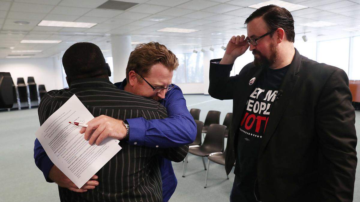 Ex-felons Lance Wissinger and Permon Thomas hug as they fill out their voter registration forms at the Lee County Supervisor of Elections office. Activist Neil Volz looks on.