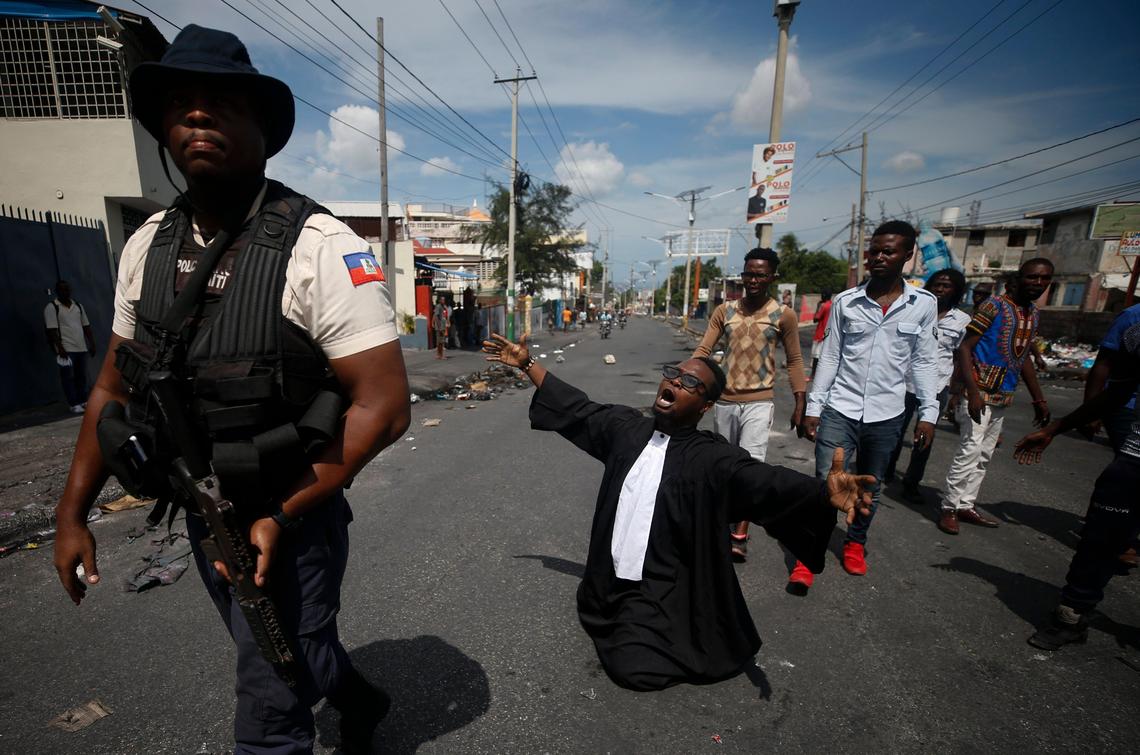 Paseus Juvensky St. Fleur, who trained as a lawyer and is now an activist working for social justice, drops to his knees as protesters trying to barricade a major road argue with police trying to stop them, in Port-au-Prince, Haiti, Wednesday, Oct. 2, 2019. 