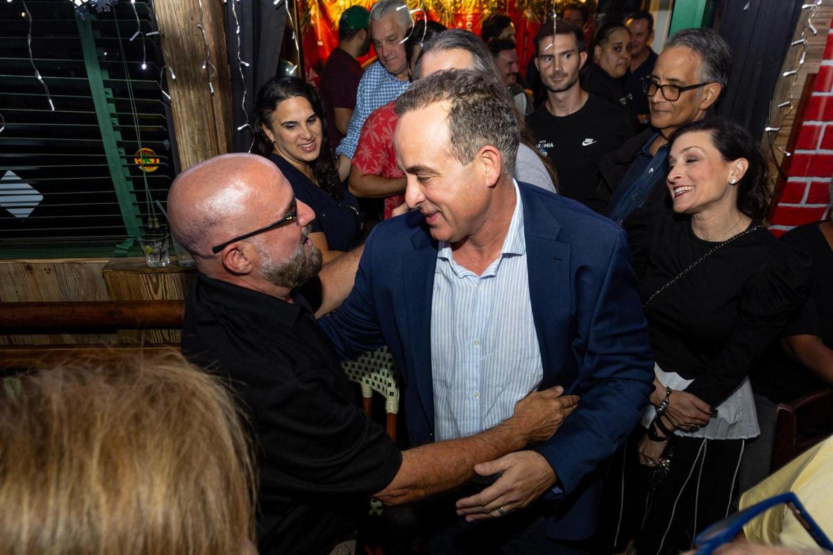 El comisionado electo Damián Pardo es abrazado por el dueño de Ball &amp; Chain Bill Fuller mientras reacciona a la noticia de haber desbancado a la actual comisionada Sabina Covo, durante una fiesta de observación de la segunda vuelta de las elecciones para el escaño de la comisión del Distrito 2 de Miami en Flanigan's, en Miami, Florida, el martes 21 de noviembre de 2023.