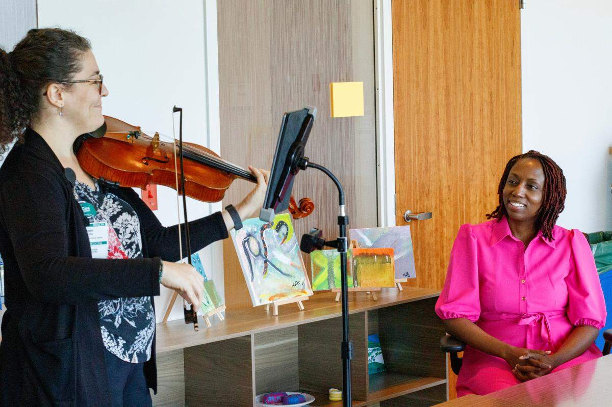 Latoya Simmons, de 42 años, sobreviviente de cáncer de mama, escucha a Robyn Savitzky, intérprete de viola y artista residente en el Baptist Hospital, tocar "How Far I'll Go" de la película de Disney "Moana", el jueves 5 de octubre de 2023. Savitzky es uno de los músicos que los pacientes de cáncer pueden solicitar para que les toque música mientras reciben tratamiento en el Instituto Oncológico de Miami.