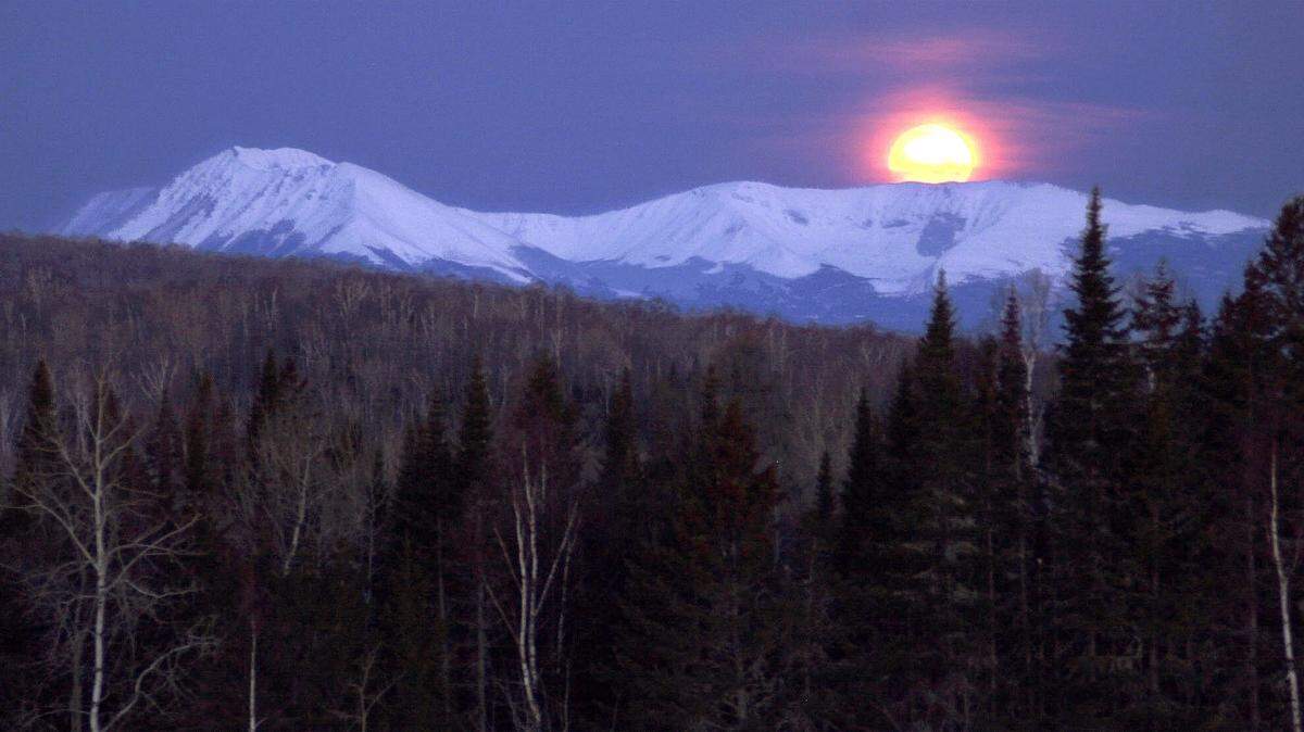 The nearly full moon sets behind the mountains of Maine’s Baxter State Park at dawn in April 2001. A rare “blue moon” — in this case, the third full moon in a season with four full moons — will rise Sunday night, experts say.