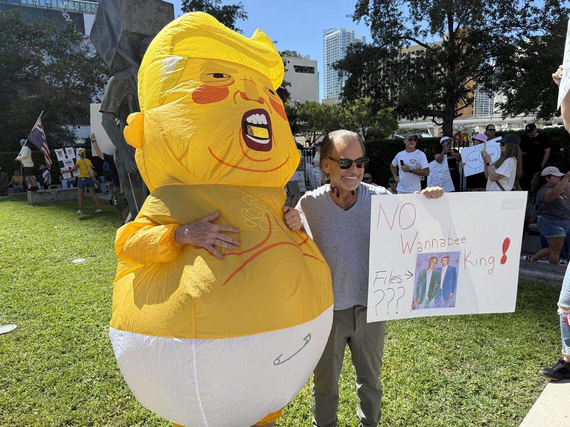 A protester dressed in an inflatable baby Trump costume poses with another protester holding a sign with an old image of Jeffrey Epstein hanging out with Donald Trump.