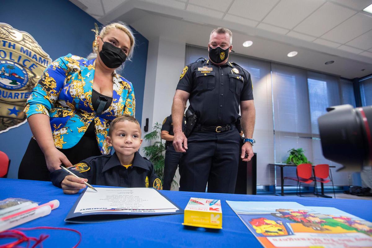 Jeremiah Valera signs the oath to be a police officer at North Miami Police Department on March 20, 2021. His mom Daniela Isaza and North Miami Police Chief Larry Juriga look on.