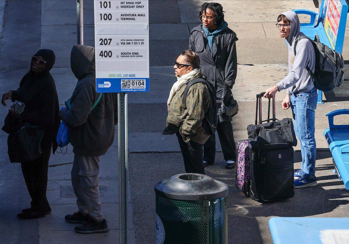 Bundled-up commuters wait at the bus stop outside Miami-Dade County on Feb. 2, 2026, in Miami, Florida.