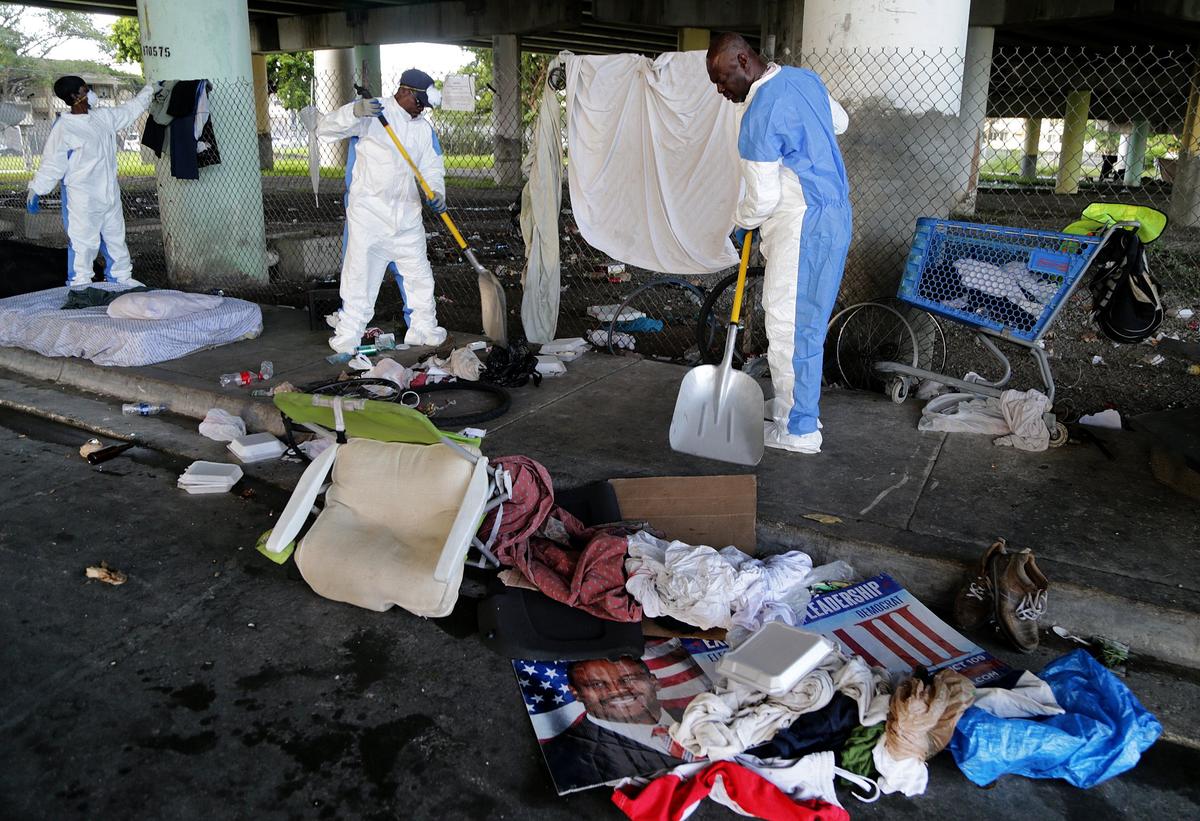 Workers wore hazmat suits as they swept bedding, clothes and trash off the sidwalk to be picked up by a garbage truck.