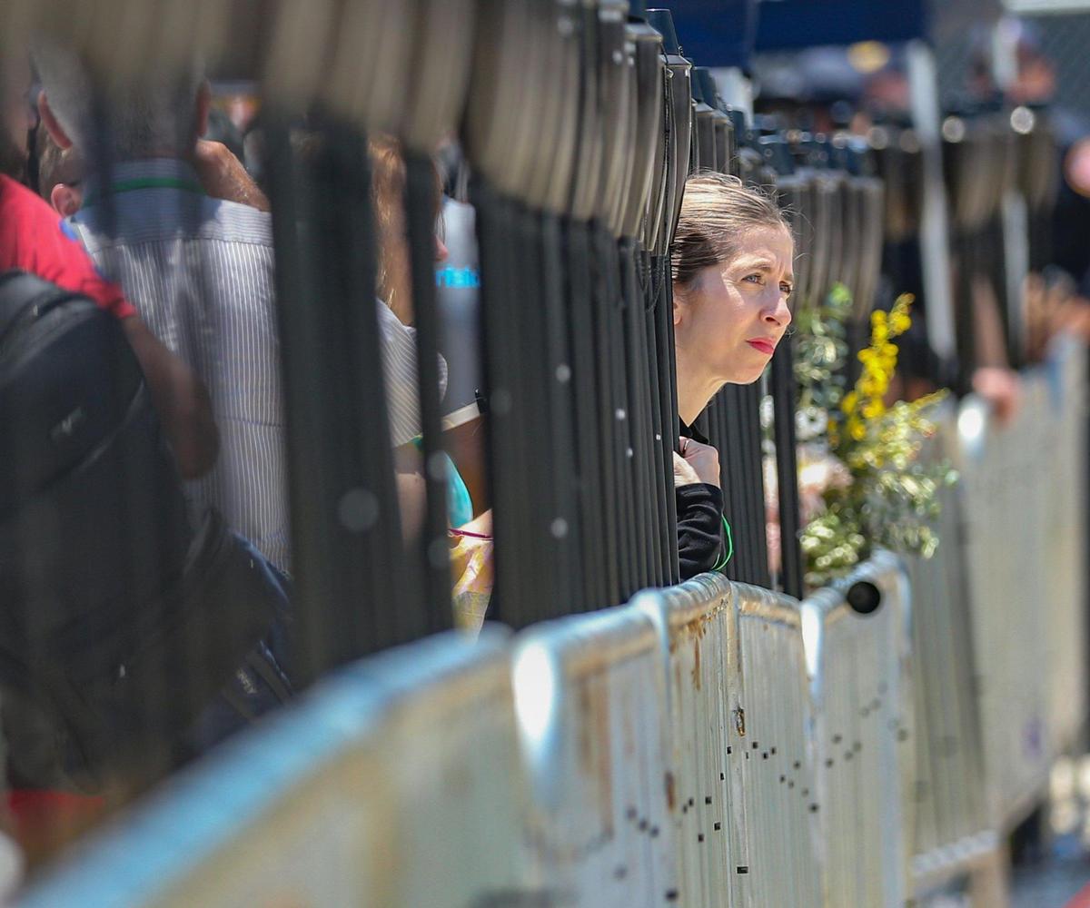 A visitor leans over a line of torches on display along a perimeter fence at the site of the collapse of Champlain Towers South in Surfside, Florida. A public memorial event was held to mark the one-year anniversary on Friday, June 24, 2022.