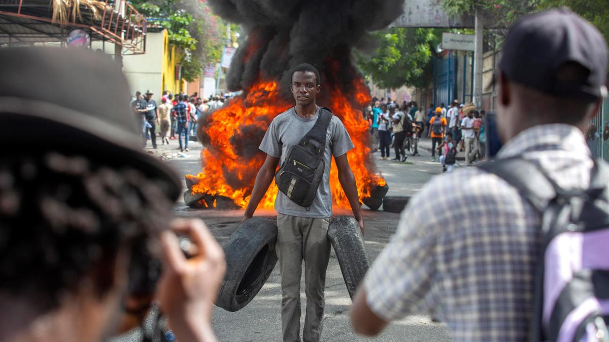 A protester, holding tires, poses for a photo in front of a burning barricade during a protest against rising insecurity in Port-au-Prince, Haiti, Thursday, Dec. 10, 2020. Port-au-Prince has seen an increase in gang violence and kidnappings.