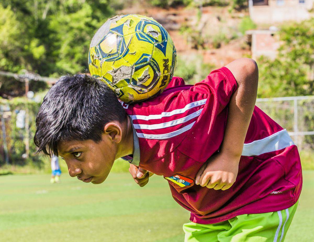 Yoangel Sanchez, 11, demonstrates for his friends how he catches and holds the soccer ball on his back at the soccer field at Villa Esperanza, Petare, Venezuela. The ball was provided by soccer organization Pasión Petare.