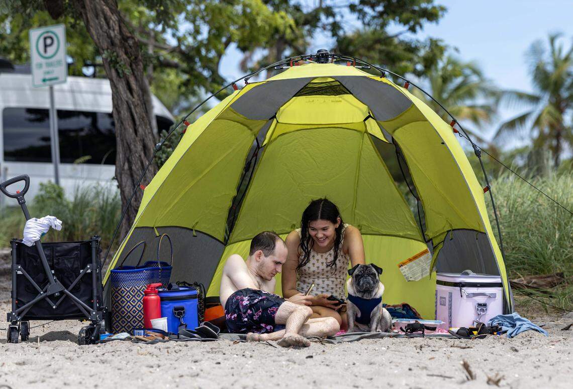 A couple and their dog enjoy the shed underneath their beach tent at the Dog Beach on Monday, September 1, 2025, in Key Biscayne, Fla.