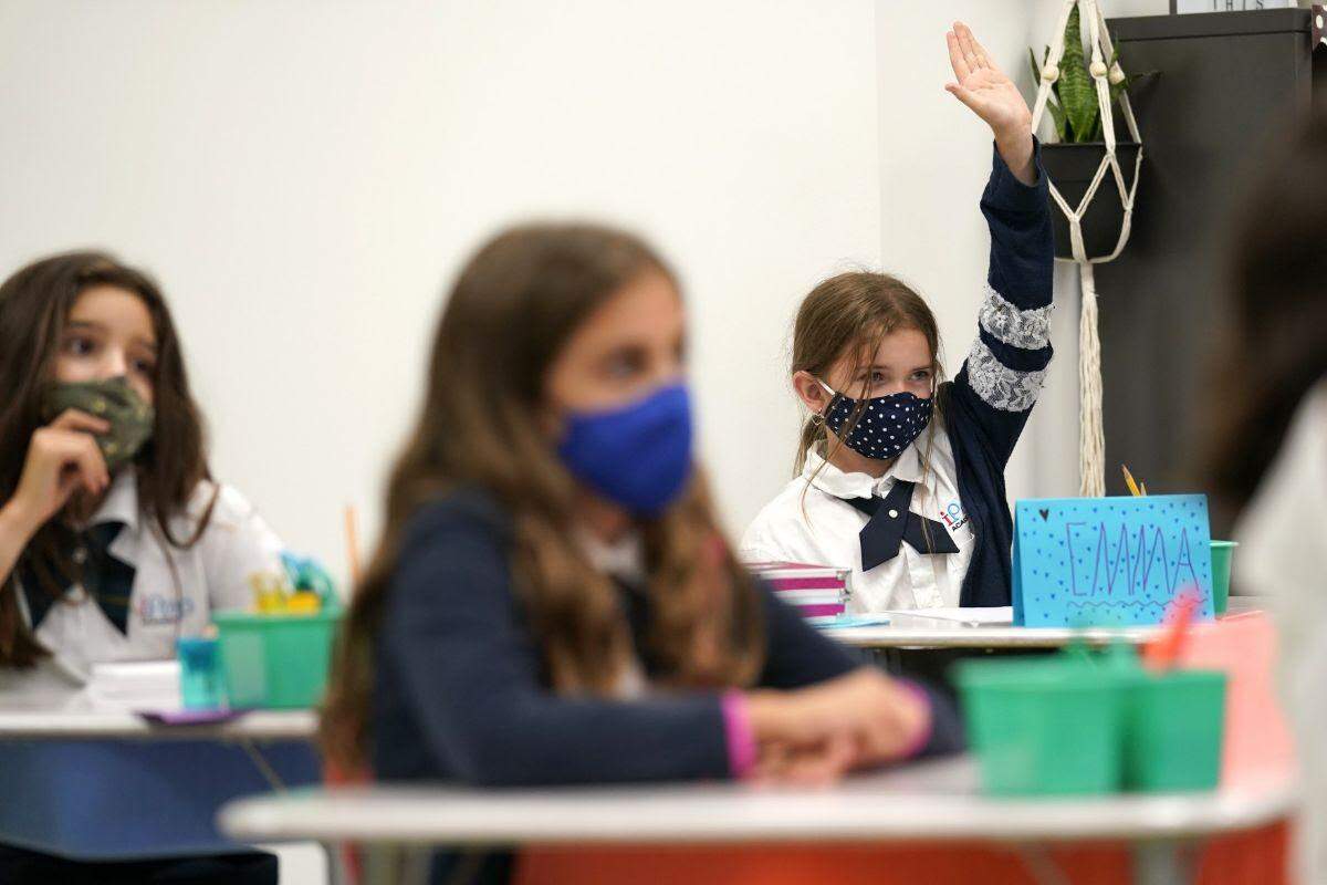 Emma Orell raises her hand in fourth grade class at iPrep Academy on the first day of school, Monday, Aug. 23, 2021, in Miami. Schools in Miami-Dade County opened Monday with a strict mask mandate to guard against coronavirus infections. Miami-Dade Schools Superintendent Alberto Carvalho is the principal of iPrep.