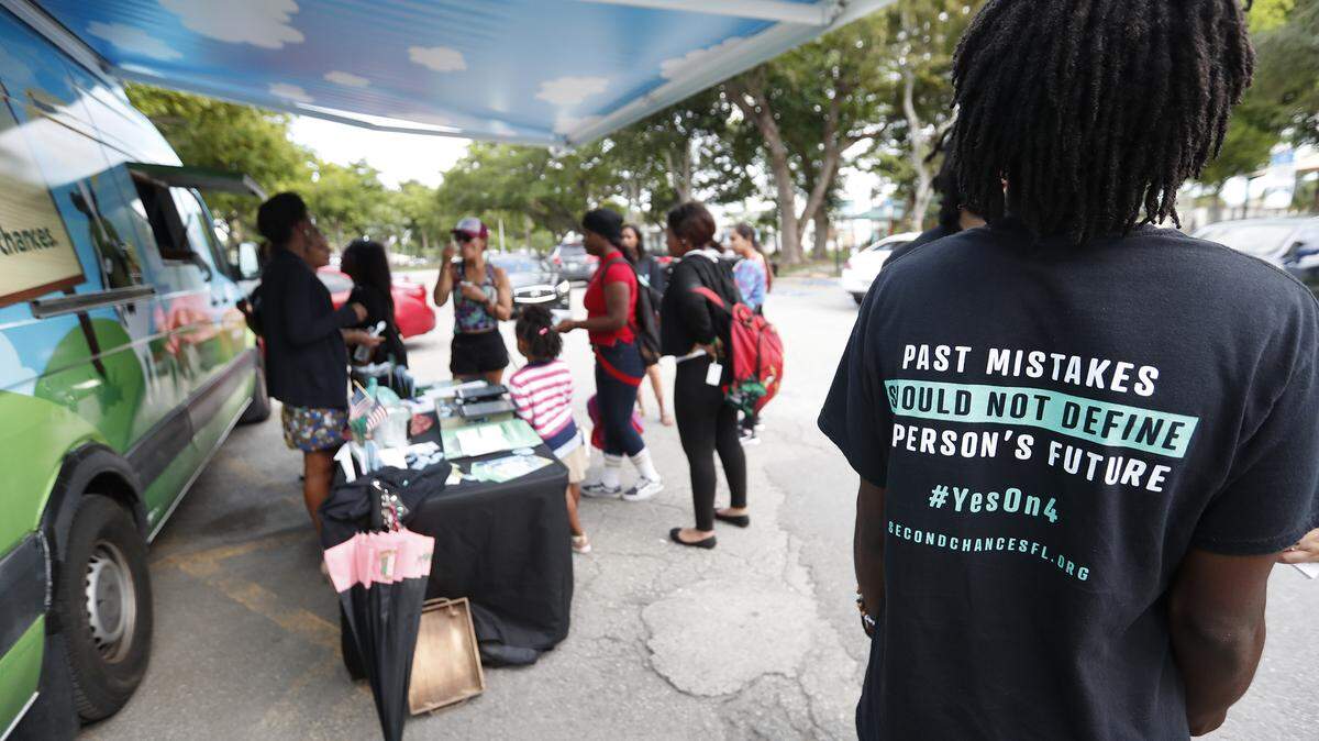 In this, Monday, Oct. 22, 2018 photo, people gather around the Ben & Jerry’s “Yes on 4” truck as they learn about Amendment 4 and eat free ice cream at Charles Hadley Park in Miami. Amendment 4, asks voters to restore the voting rights of people with past felony convictions. More than 1.5 million adults in Florida are ineligible to vote because they have felony convictions.   (AP Photo/Wilfredo Lee)
