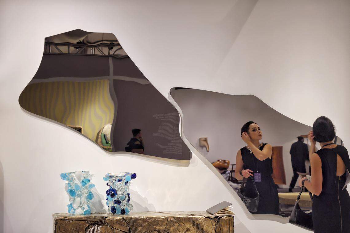 Miami Beach, FL, December 2, 2025 - Katja Alekseeva of David Gill Gallery London preps her hair in front of the large mirror (artwork) as Design Miami XX opens its doors during Miami Art Week on Tuesday, December 2, 2025, in Miami Beach, Florida.