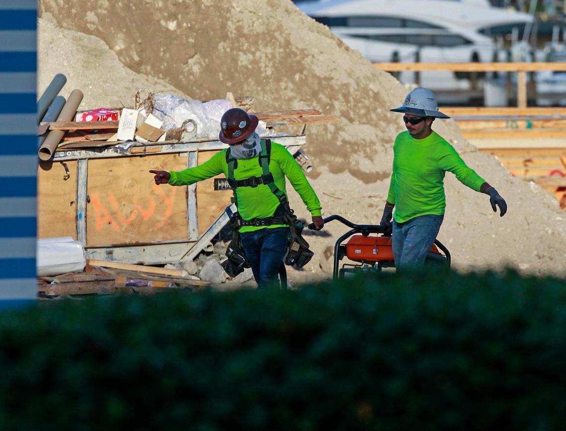 Two workers at the Monaco Yacht Club and Residences construction site in Miami Beach carry a generator on Thursday, April 2, 2020.