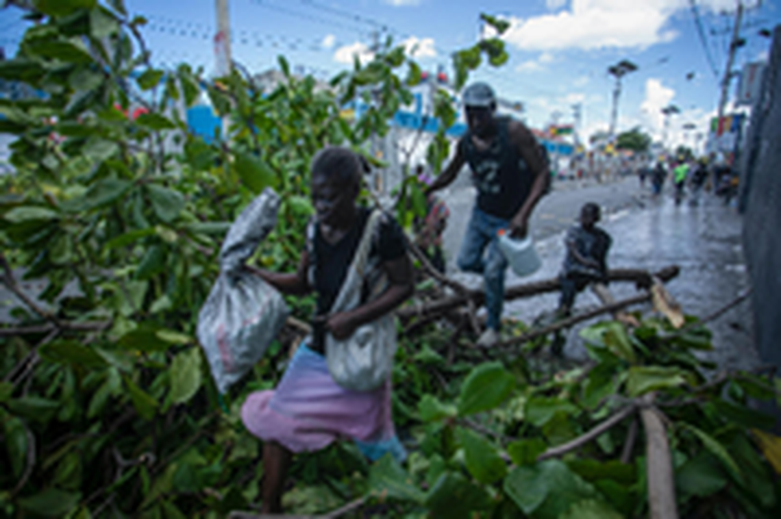 People walk over a downed tree set up as a barricade during a protest demanding the resignation of Prime Minister Ariel Henry in the Delmas area of Port-au-Prince, Haiti, Monday, Oct. 10, 2022.