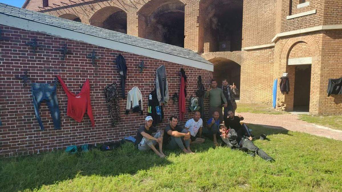 A group of men sit by a brick wall at Fort Jefferson on Garden Key within the Dry Tortugas National Park, with laundry hung to dry behind them. The National Park Service closed the Tortugas Sunday, Jan. 1, 2022, after almost 500 Cuban migrants arrived there over the course of several days.
