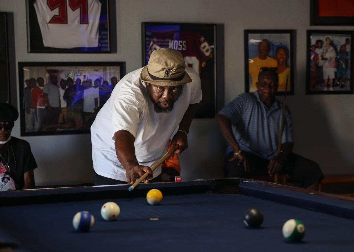 Terrence “Uncle Tee” Smith, the owner of Barbara and Kirk Barbecue, which doubles as a hangout and pool hall. Smith plays pool as locals look on inside Barbara and Kirk’s while the area undergoes revitalization in Miami’s Liberty City neighborhood on Wednesday, May 6, 2021.